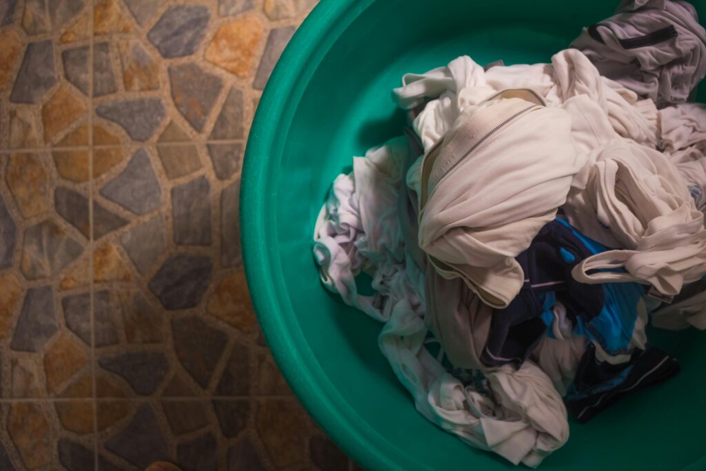 pexels-photo-4992081-4992081 Top view of a laundry basket filled with crumpled clothes on a tiled floor.