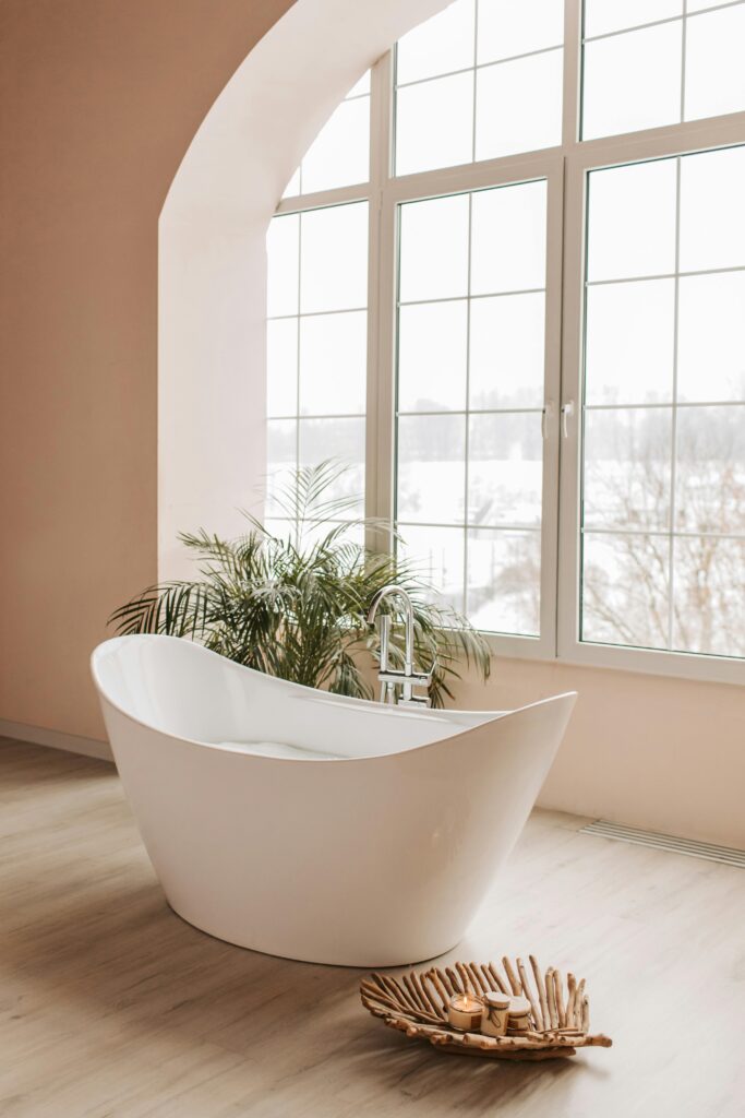 pexels-photo-6634896-6634896 Elegant freestanding bathtub in a bright, minimalist bathroom with large windows and potted plants.