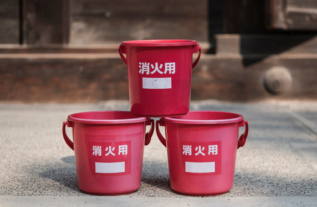 Set of red fire buckets with Japanese text in an outdoor setting.